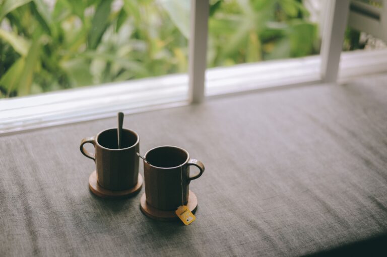 Cozy scene of two ceramic cups on a table with green background, suggesting relaxation.