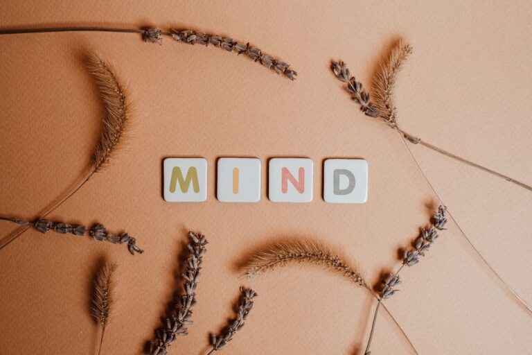 Flat lay of the word 'MIND' surrounded by dried flowers on a warm backdrop.